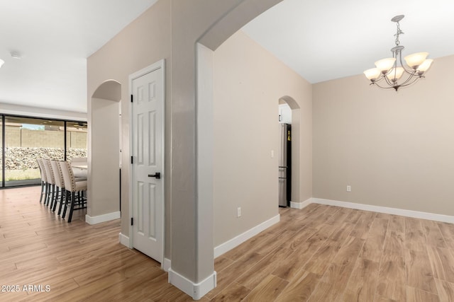 interior space featuring arched walkways, baseboards, a chandelier, and light wood-type flooring