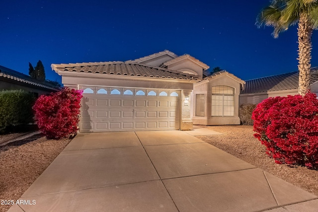 mediterranean / spanish home featuring concrete driveway, an attached garage, a tiled roof, and stucco siding