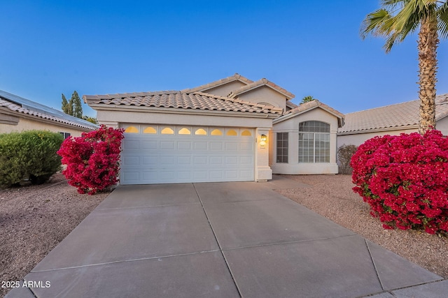 mediterranean / spanish house featuring driveway, a tile roof, a garage, and stucco siding