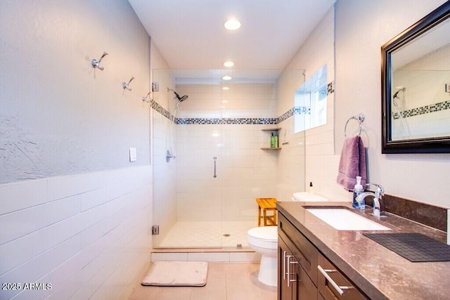 bathroom with toilet, tile walls, tile patterned floors, a shower with shower door, and vanity