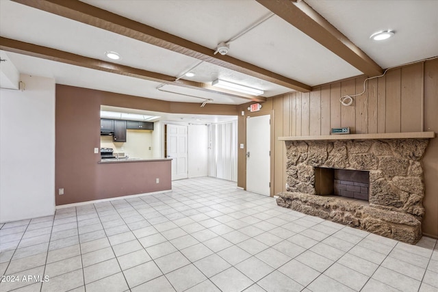 unfurnished living room featuring a fireplace, beam ceiling, tile patterned flooring, and wood walls