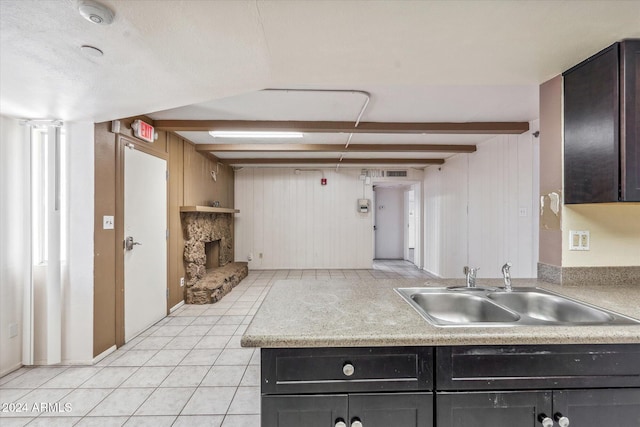 kitchen featuring a stone fireplace, sink, light tile patterned floors, a textured ceiling, and beam ceiling