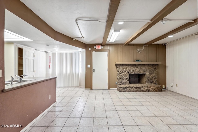 unfurnished living room featuring a textured ceiling, beam ceiling, light tile patterned floors, a fireplace, and wood walls