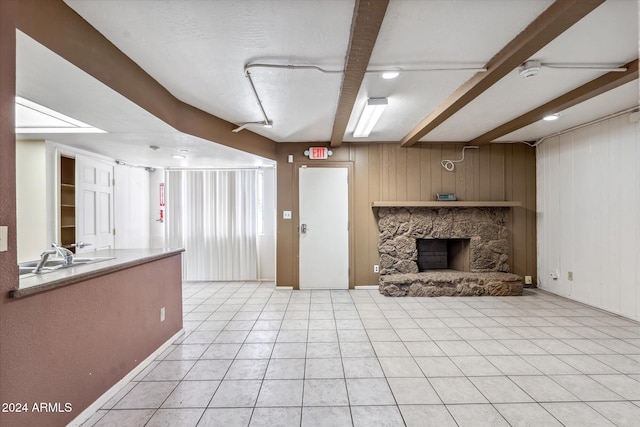 unfurnished living room featuring beam ceiling, a stone fireplace, a textured ceiling, wooden walls, and light tile patterned flooring