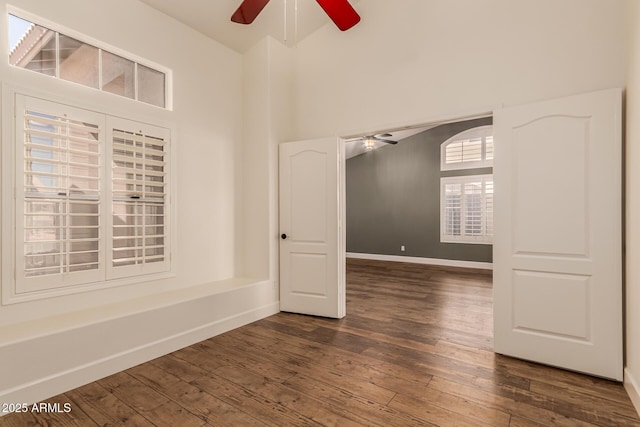 empty room featuring ceiling fan, a towering ceiling, and dark hardwood / wood-style flooring