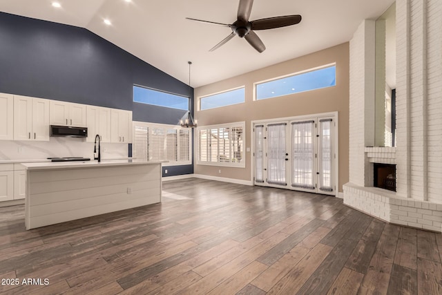 unfurnished living room with dark wood-type flooring, high vaulted ceiling, ceiling fan with notable chandelier, and a brick fireplace