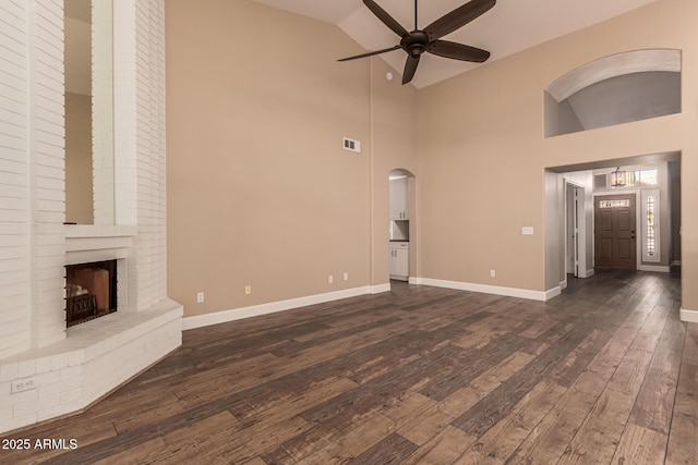 unfurnished living room featuring ceiling fan, dark hardwood / wood-style floors, high vaulted ceiling, and a brick fireplace