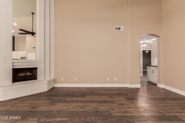 unfurnished living room with ceiling fan, dark hardwood / wood-style flooring, a brick fireplace, and a high ceiling