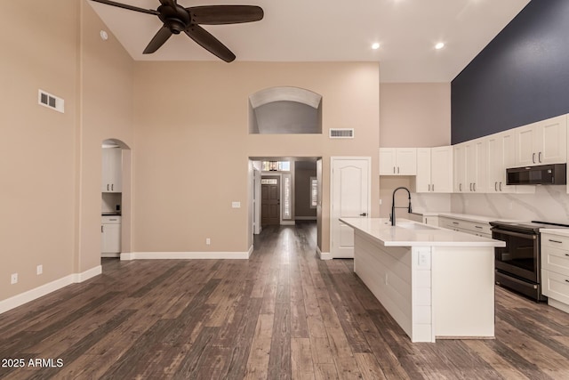 kitchen with a towering ceiling, sink, white cabinets, a kitchen island with sink, and electric range