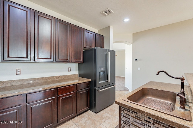 kitchen featuring black refrigerator with ice dispenser, a sink, arched walkways, dark brown cabinetry, and visible vents