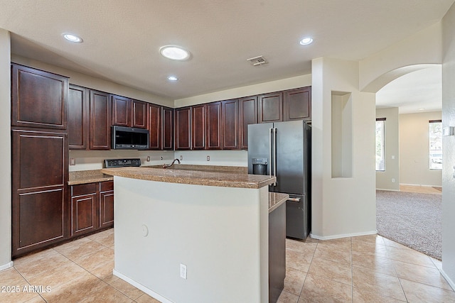 kitchen featuring light tile patterned floors, arched walkways, fridge with ice dispenser, stainless steel microwave, and visible vents