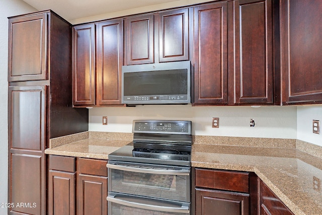 kitchen featuring stainless steel microwave, range with two ovens, light stone counters, and dark brown cabinets