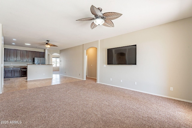 unfurnished living room with light colored carpet, ceiling fan, arched walkways, and baseboards
