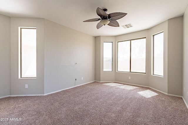 carpeted spare room with a wealth of natural light, a ceiling fan, visible vents, and baseboards