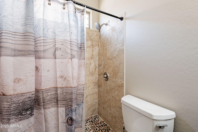 bathroom with a textured wall, toilet, and tiled shower