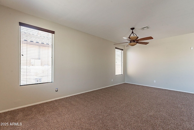 spare room with dark carpet, a ceiling fan, a healthy amount of sunlight, and visible vents