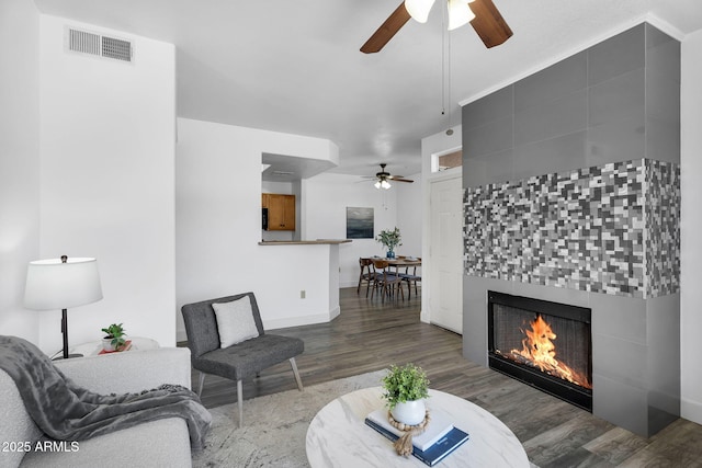 living area with ceiling fan, wood finished floors, a tiled fireplace, and baseboards