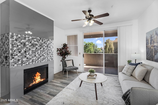 living room featuring a ceiling fan, wood finished floors, a tiled fireplace, and baseboards
