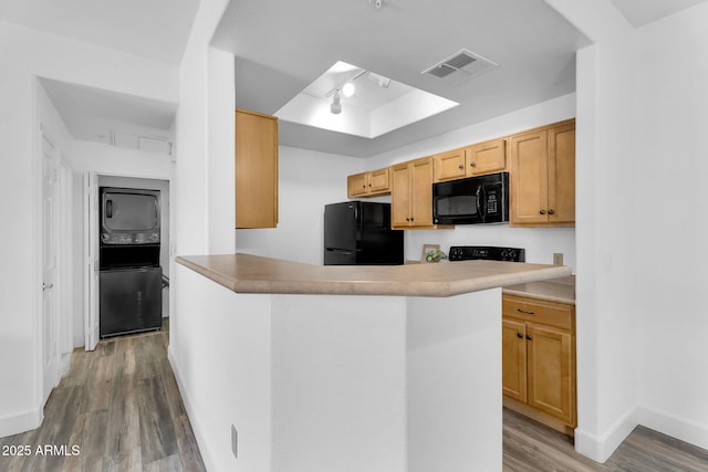 kitchen with black appliances, stacked washing machine and dryer, a raised ceiling, wood finished floors, and baseboards