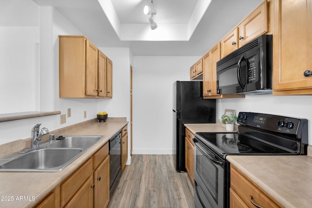 kitchen with black appliances, a sink, a tray ceiling, light wood-style flooring, and rail lighting