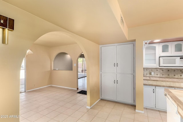 kitchen with white microwave, backsplash, light countertops, light tile patterned floors, and white cabinets