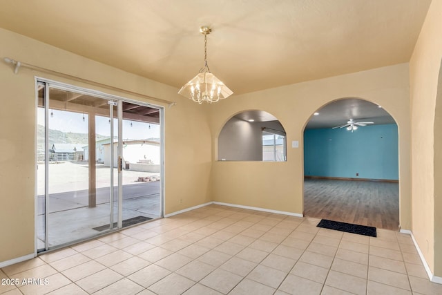 unfurnished room with light tile patterned floors, baseboards, arched walkways, and ceiling fan with notable chandelier