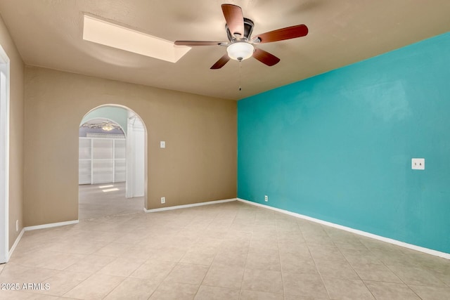 spare room featuring a ceiling fan, a skylight, arched walkways, and baseboards