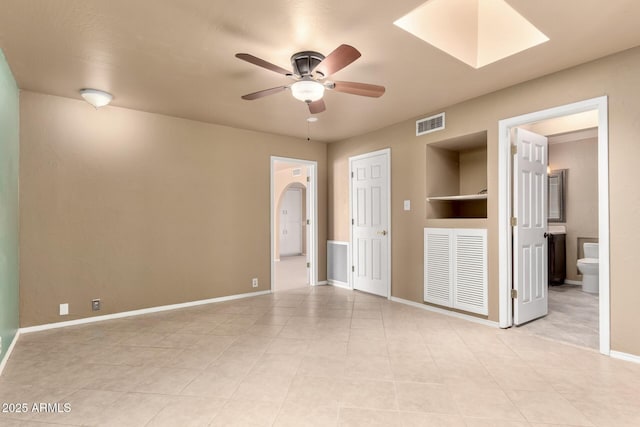 unfurnished room featuring baseboards, visible vents, arched walkways, and ceiling fan