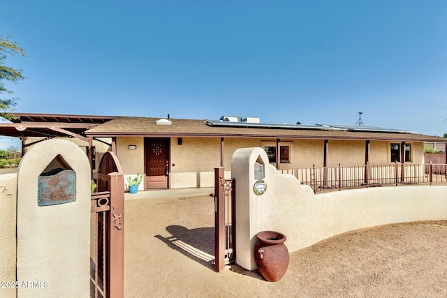 ranch-style house featuring solar panels, fence, and stucco siding