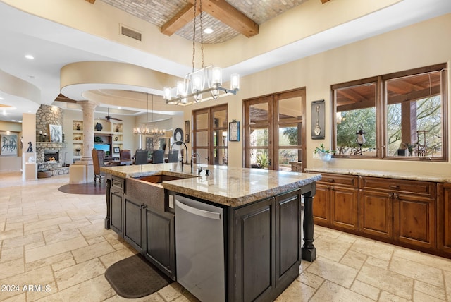 kitchen featuring a stone fireplace, dishwasher, an island with sink, beam ceiling, and decorative light fixtures