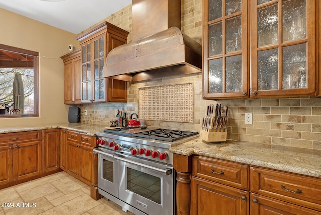 kitchen featuring light stone counters, custom exhaust hood, double oven range, and backsplash