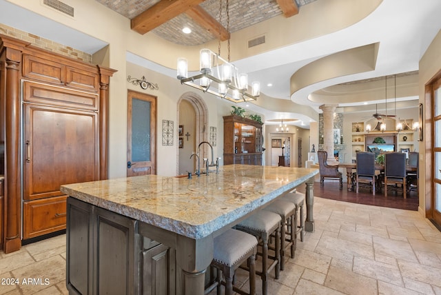 kitchen featuring decorative columns, pendant lighting, a large island, and beamed ceiling