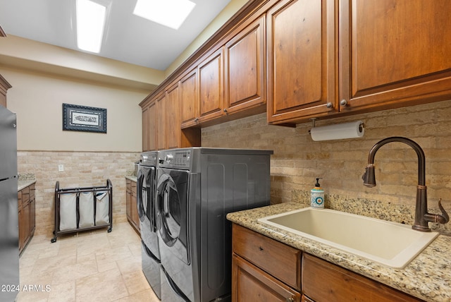 laundry area featuring tile walls, cabinets, washer and clothes dryer, and sink