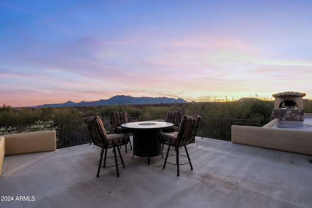 patio terrace at dusk featuring an outdoor stone fireplace and a mountain view