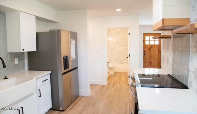 kitchen with stainless steel fridge with ice dispenser, a sink, white cabinets, light wood-style floors, and backsplash