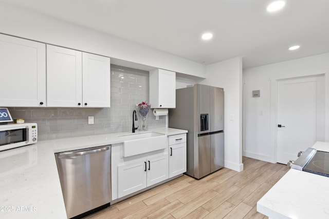 kitchen featuring a sink, backsplash, appliances with stainless steel finishes, and white cabinetry