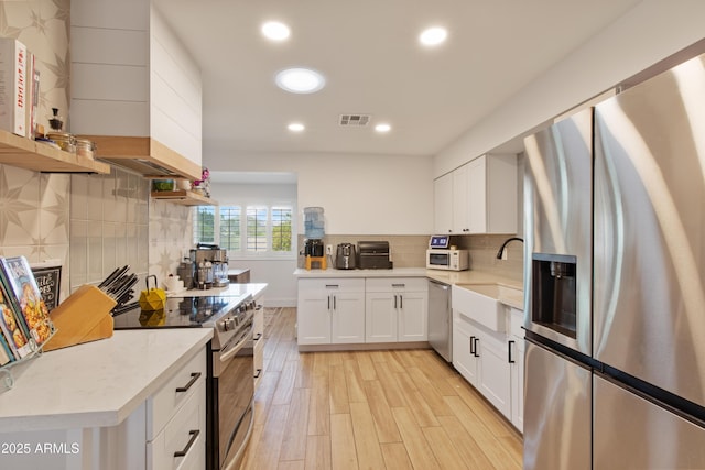 kitchen with visible vents, appliances with stainless steel finishes, light wood-style floors, white cabinetry, and a sink