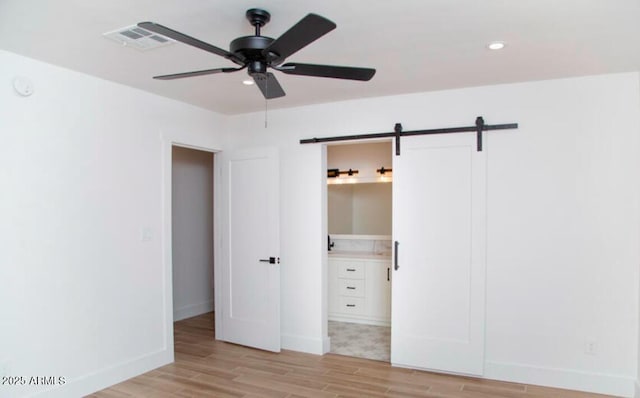 unfurnished bedroom featuring baseboards, visible vents, recessed lighting, a barn door, and light wood-type flooring