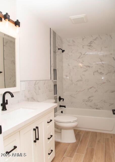 bathroom with vanity, wood finish floors, shower / tub combination, toilet, and tile walls