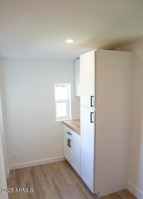 kitchen featuring white cabinets, baseboards, light wood-type flooring, and wood counters