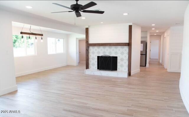 unfurnished living room featuring light wood finished floors, recessed lighting, a fireplace with raised hearth, and ceiling fan