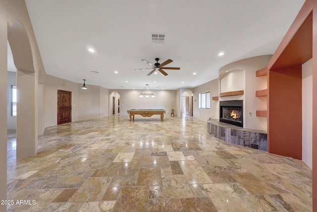 28758 N Ashbrook Ln, San Tan Valley, AZ 85144 - unfurnished living room with arched walkways, a tiled fireplace, billiards table, ceiling fan, and stone finish floors