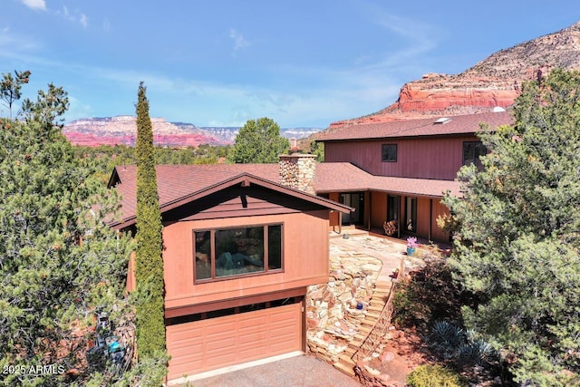 chalet / cabin featuring roof with shingles, a chimney, an attached garage, and a mountain view