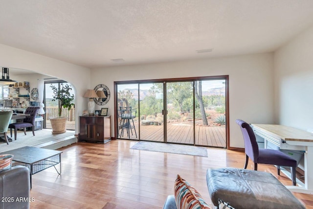 living room featuring arched walkways, a healthy amount of sunlight, a textured ceiling, and wood finished floors