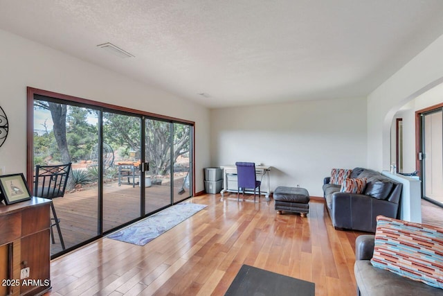 living room with a textured ceiling, visible vents, arched walkways, and light wood-style flooring