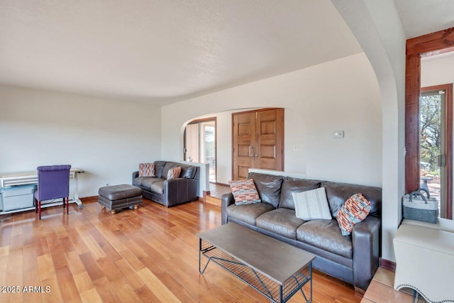 living area with light wood-style flooring, arched walkways, and baseboards