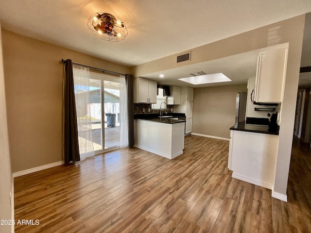 kitchen featuring sink, light hardwood / wood-style flooring, white cabinetry, backsplash, and kitchen peninsula