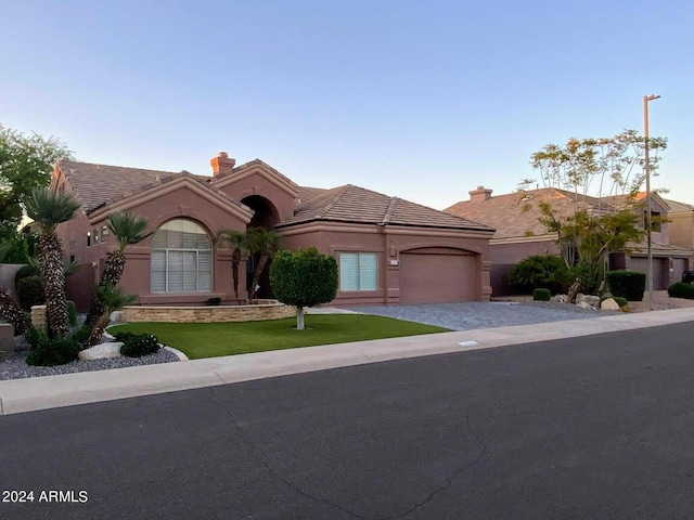 mediterranean / spanish house featuring a garage, a chimney, a tiled roof, decorative driveway, and stucco siding