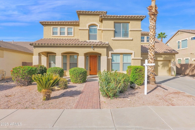 mediterranean / spanish home with a garage, a tiled roof, concrete driveway, and stucco siding