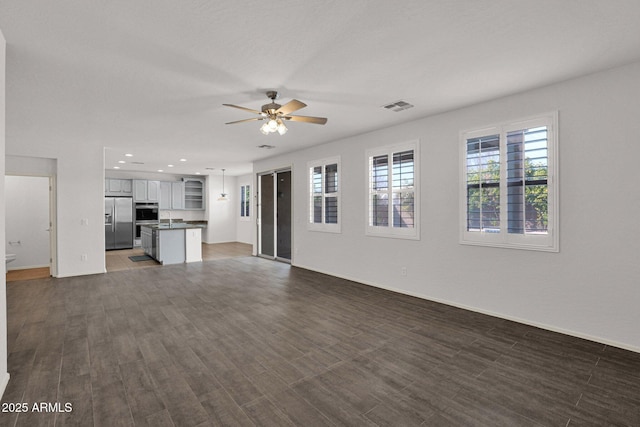 unfurnished living room featuring a sink, ceiling fan, visible vents, and dark wood-type flooring